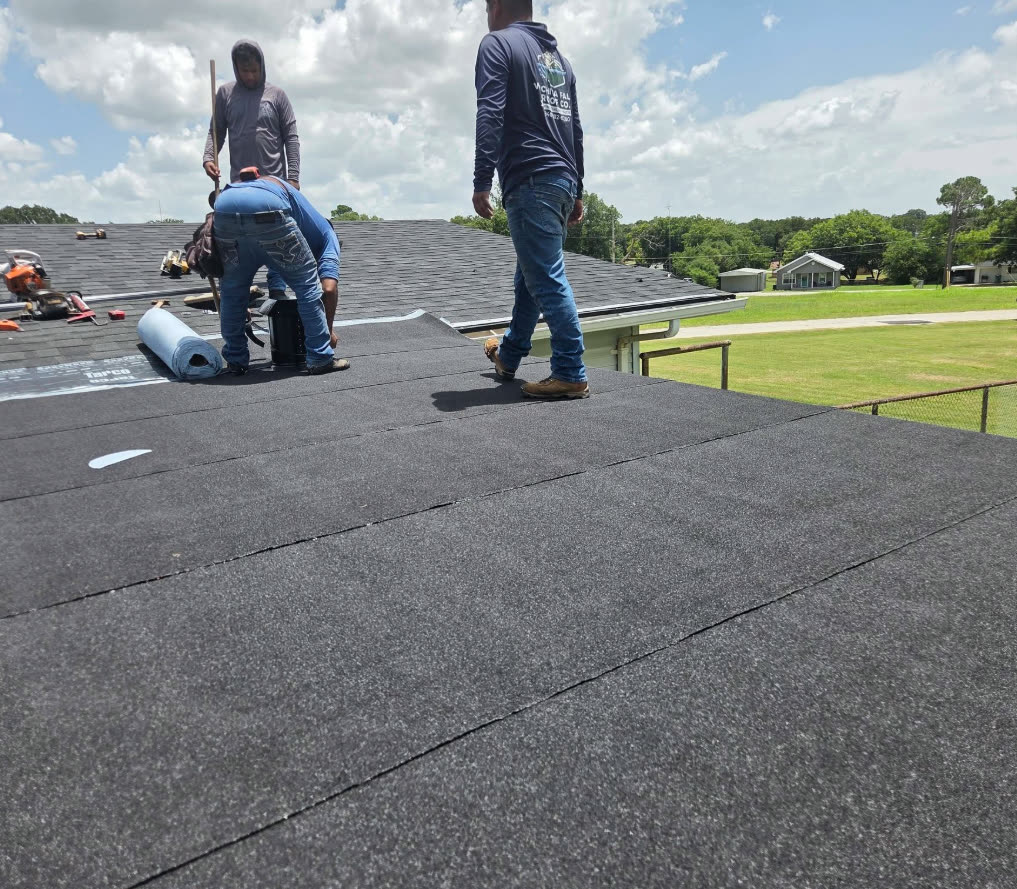 Three crew members laying underlayment on a roof